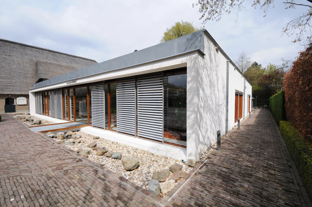 Modern laagbouwgebouw aan de Charloisse Lagedijk met grote ramen en horizontale zonwering, omringd door een bestrate wandelweg en siergrind.